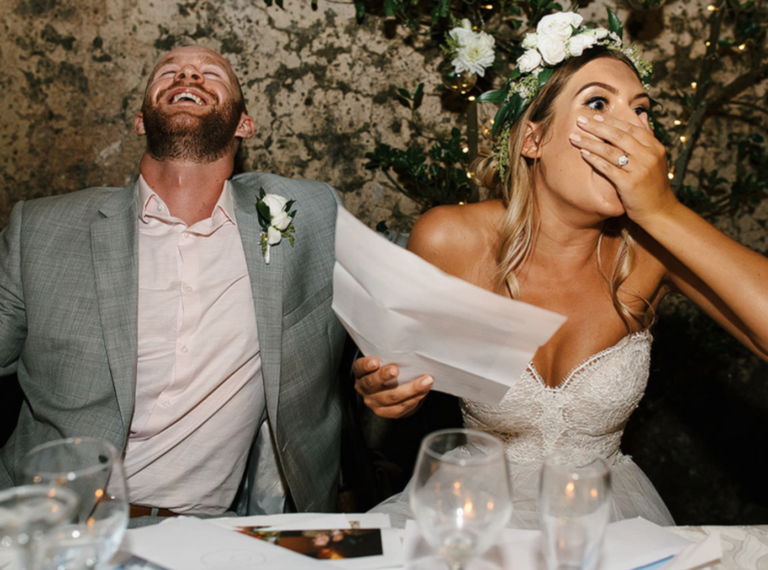 Wedding couple laughing while listening to a speech delivered by a guest.